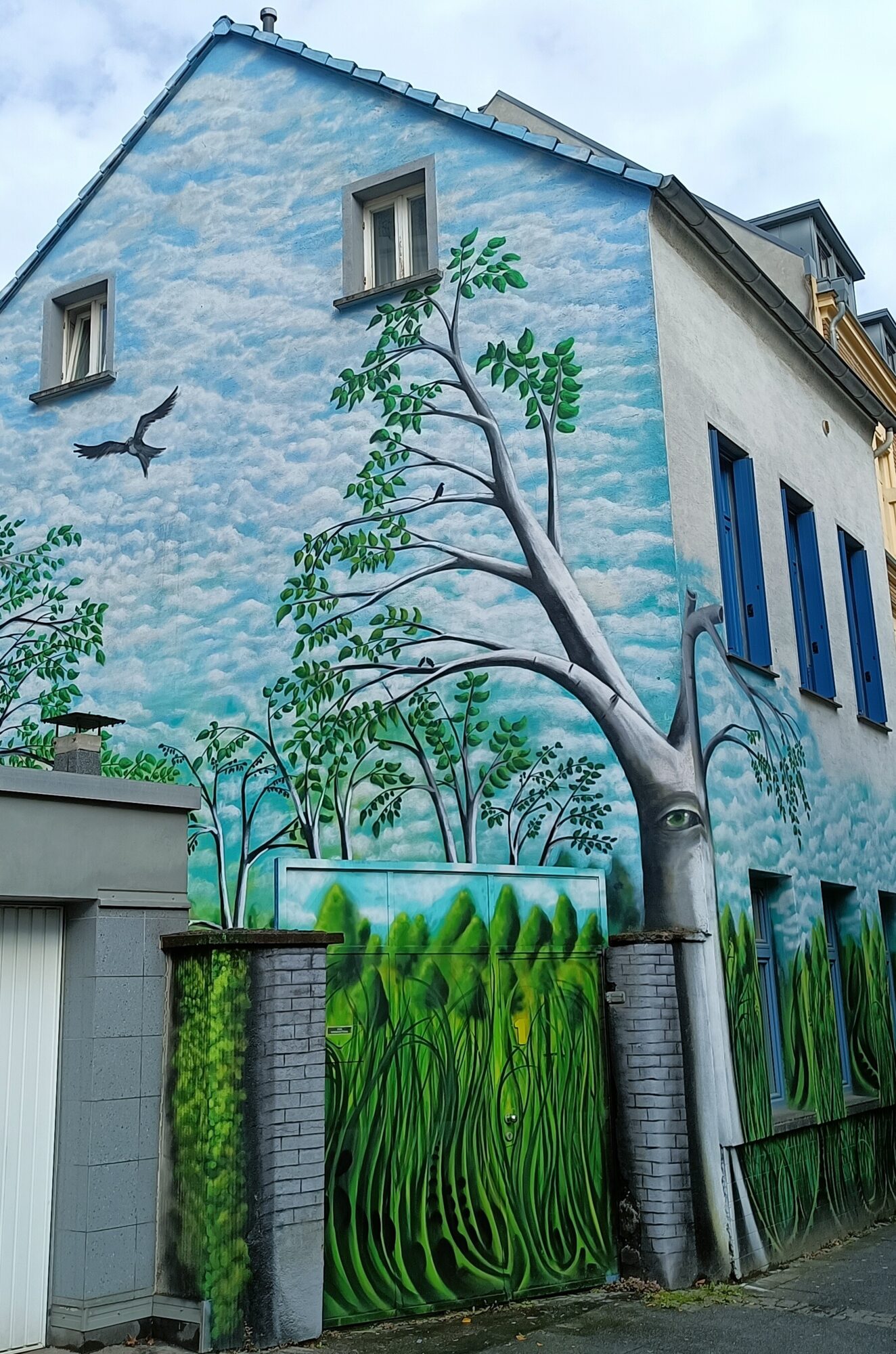 Gable of sky and a tree with an eye — Street art in Köln