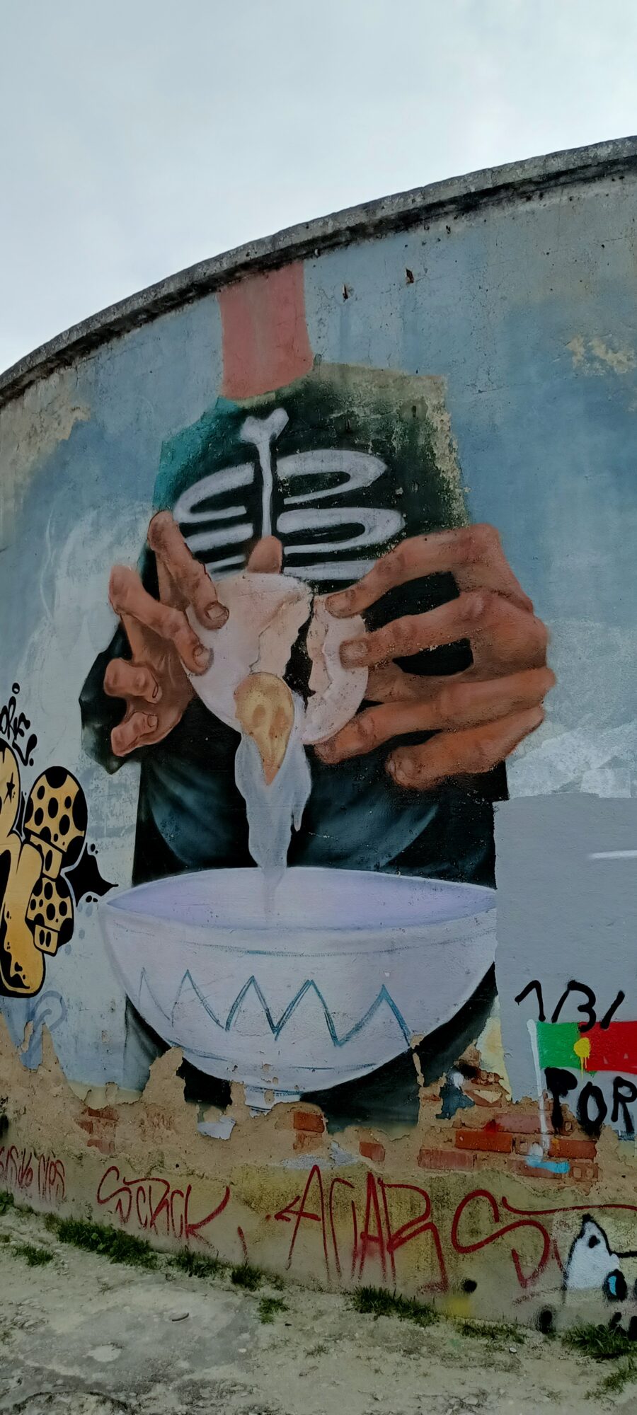Mains cassant un œuf au crâne — Street art à Almada