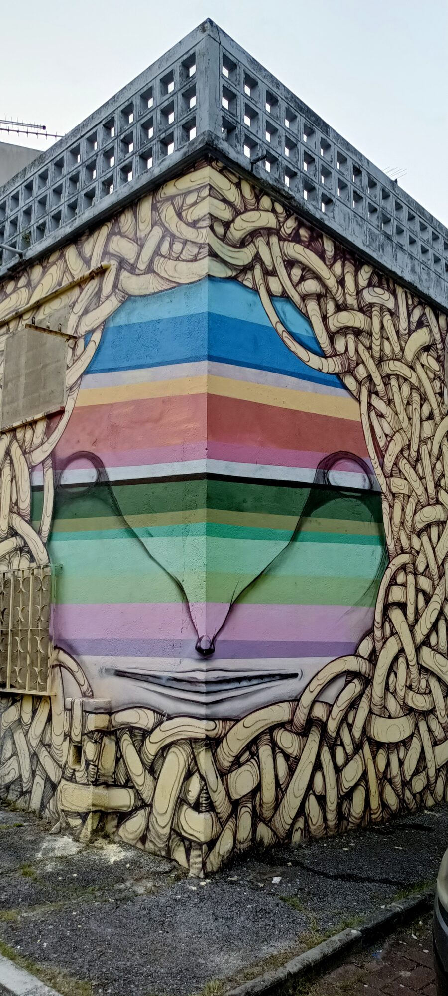 Visage arc-en-ciel enveloppant l'angle du mur — Street art à Lisboa