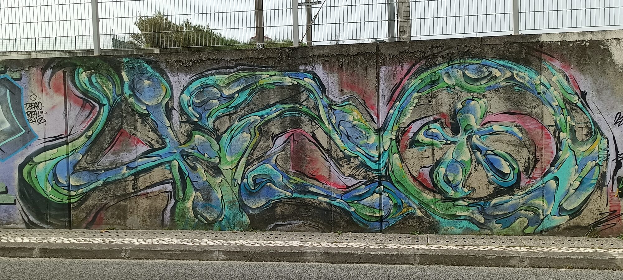 Lettrage fluide vert et bleu sur béton brut — Street art de Obit à Lisboa