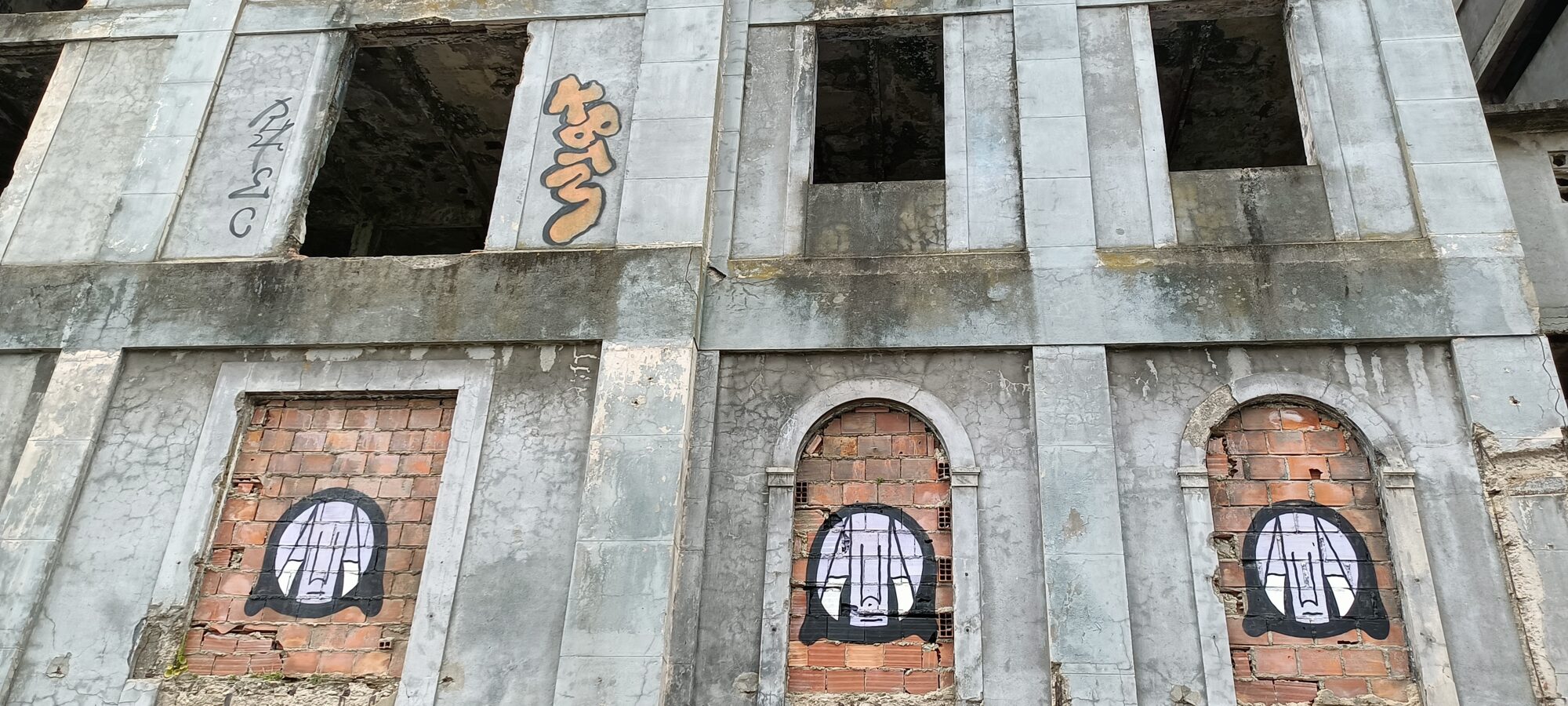 Three Faces in the Bricked-Up Openings — Street art in Almada
