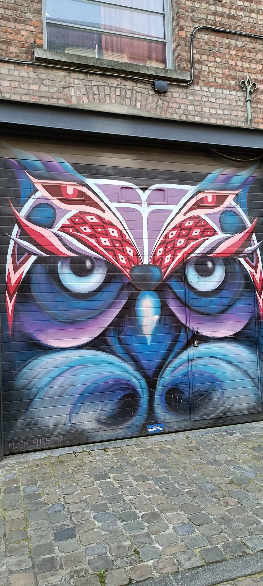 Stylised owl on a garage door — Street art by Muga in Bruxelles