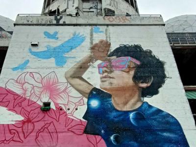 Jeune homme rêveur entre fleurs et cité onirique — Street art de MATE à Berlin