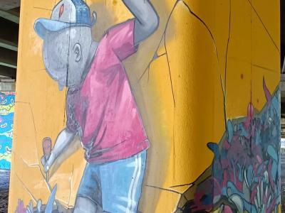 Child Painter Cracking the Yellow Pillar — Street art in Rīga