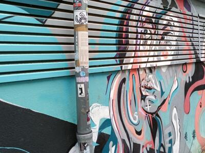 Face with coral and turquoise ribbons — Street art in Köln