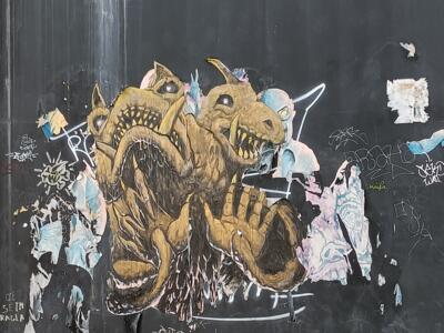 Créature dorée bicéphale sur bardage noir — Street art à Marseille