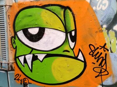 Green cyclops monster on orange — Street art in Marseille