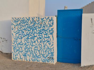 Blue Arabic calligraphy by the door — Street art in Aghir
