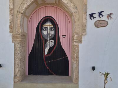 Femme voilée à la porte rose par Jihene Tellidora — Street art de Jihene Tellidora à Erriadh